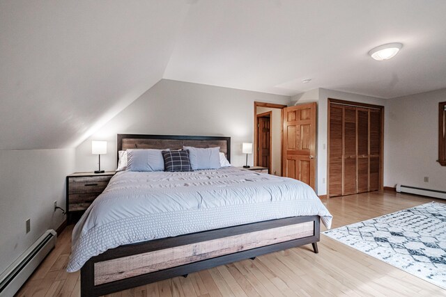 bedroom featuring light hardwood / wood-style floors, vaulted ceiling, a baseboard heating unit, and a closet