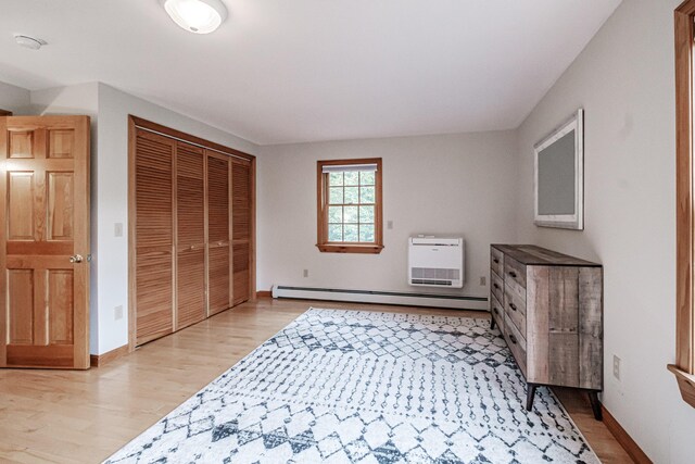 bedroom featuring light hardwood / wood-style flooring, heating unit, a closet, and baseboard heating