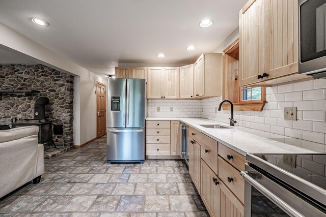 kitchen with light brown cabinetry, sink, stainless steel appliances, and tasteful backsplash