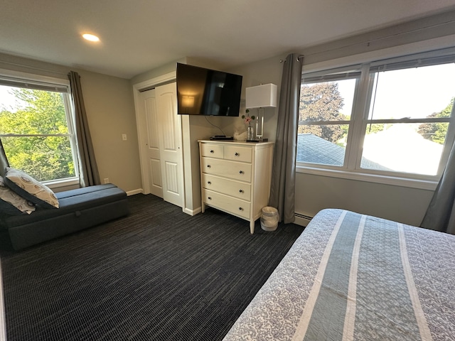 unfurnished bedroom featuring baseboard heating, dark carpet, and a closet