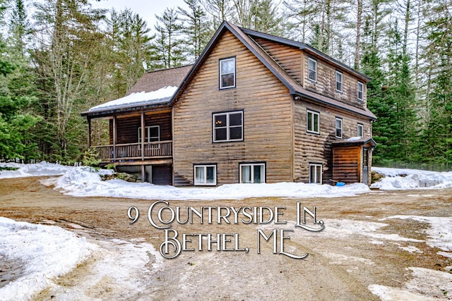snow covered rear of property with an attached garage and log veneer siding