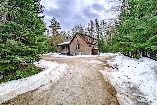 view of snow covered exterior with an attached garage, a view of trees, and driveway