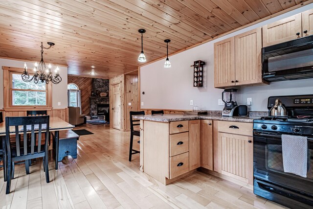 kitchen with wood walls, light brown cabinetry, decorative light fixtures, and black appliances