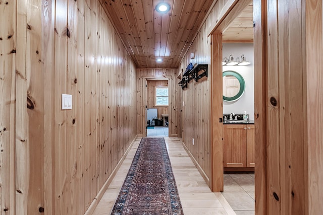 corridor featuring wooden walls, wood ceiling, a sink, and light wood finished floors