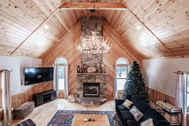 living room featuring wooden walls, a stone fireplace, an inviting chandelier, and wood finished floors