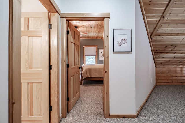 hallway featuring light carpet, wood ceiling, and baseboards