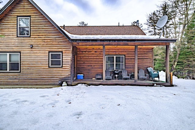 snow covered back of property with a shingled roof and log veneer siding