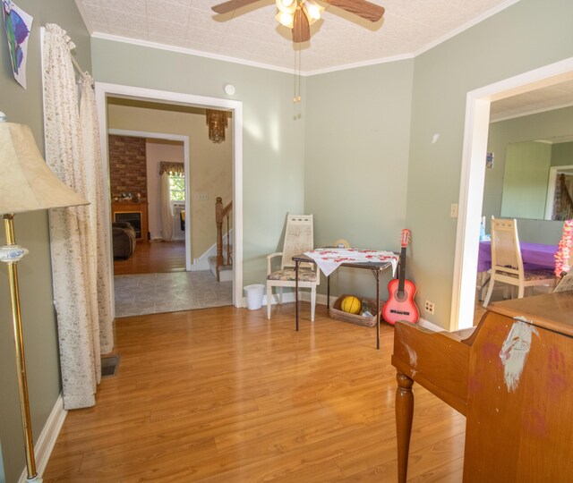 recreation room featuring a fireplace, crown molding, light hardwood / wood-style flooring, and ceiling fan