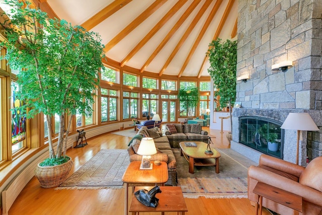 living room featuring light hardwood / wood-style flooring, a stone fireplace, high vaulted ceiling, and beam ceiling