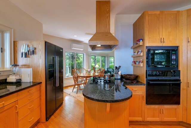 kitchen featuring exhaust hood, black appliances, a center island, a wall unit AC, and light wood-type flooring