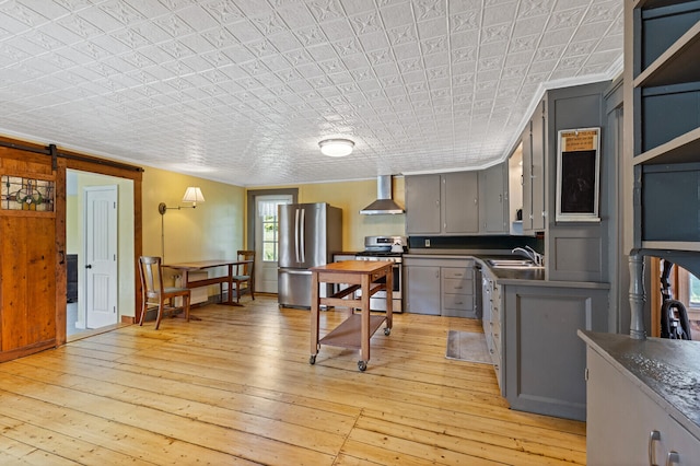 kitchen featuring light hardwood / wood-style flooring, appliances with stainless steel finishes, gray cabinets, a barn door, and wall chimney range hood