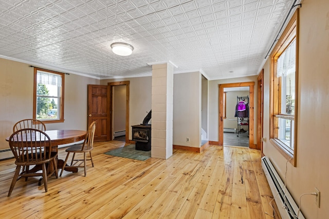 dining room with a wood stove, a baseboard radiator, ornamental molding, and light wood-type flooring