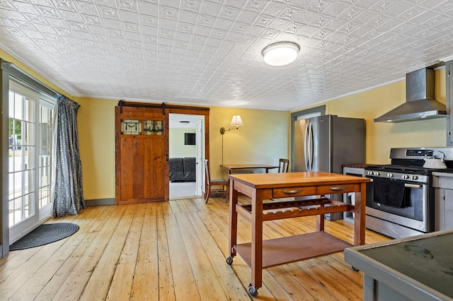 kitchen featuring a healthy amount of sunlight, a barn door, light hardwood / wood-style flooring, stainless steel appliances, and wall chimney range hood