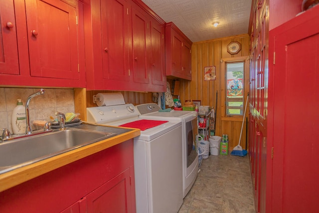 laundry area with wood walls, cabinets, washer and dryer, and sink