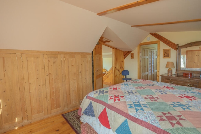 bedroom with vaulted ceiling with beams, wood walls, and hardwood / wood-style flooring