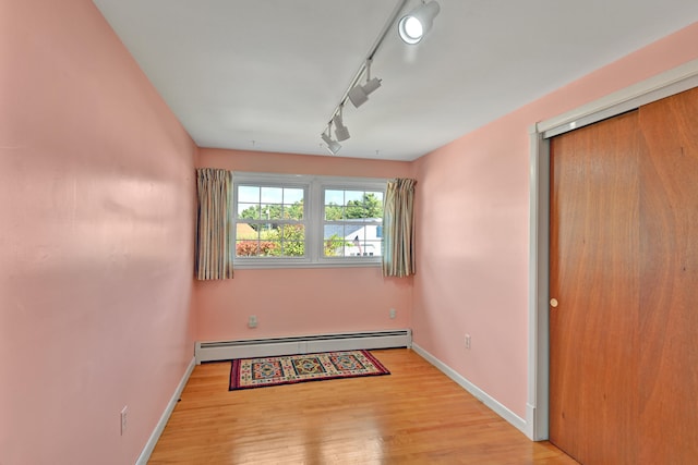 empty room with a baseboard radiator, light hardwood / wood-style flooring, and rail lighting