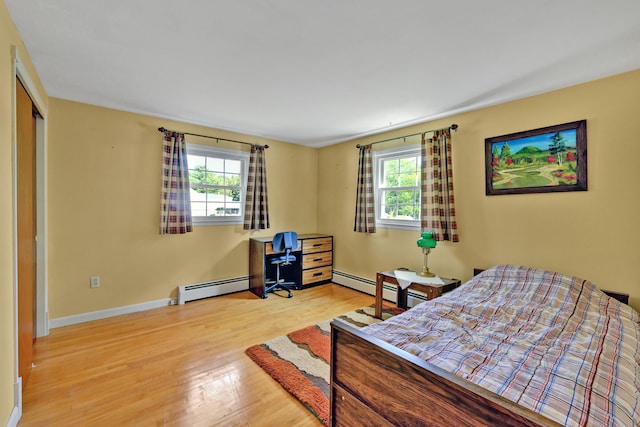 bedroom featuring baseboard heating, light wood-type flooring, a closet, and multiple windows