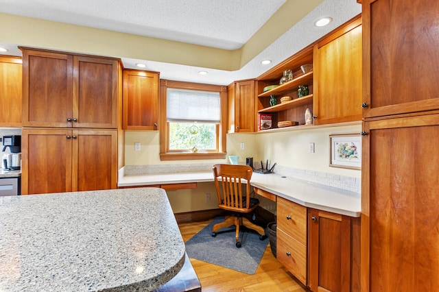 interior space featuring a textured ceiling, built in desk, light stone countertops, and light hardwood / wood-style floors