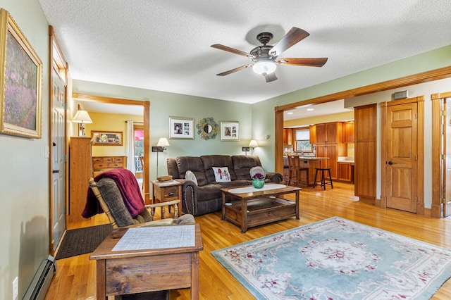 living room with ceiling fan, a baseboard radiator, light hardwood / wood-style floors, and a textured ceiling