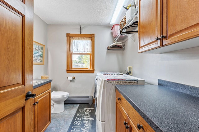 interior space with toilet, vanity, a textured ceiling, washing machine and dryer, and a baseboard heating unit