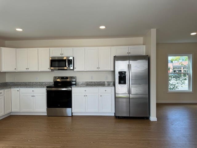 kitchen with dark wood-type flooring, stainless steel appliances, dark stone countertops, and white cabinets