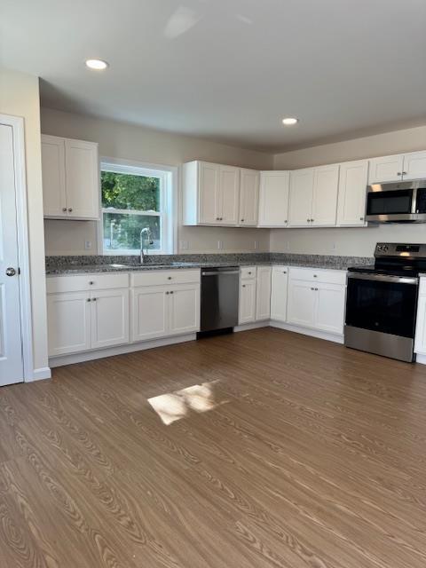 kitchen with appliances with stainless steel finishes, white cabinetry, wood-type flooring, and sink