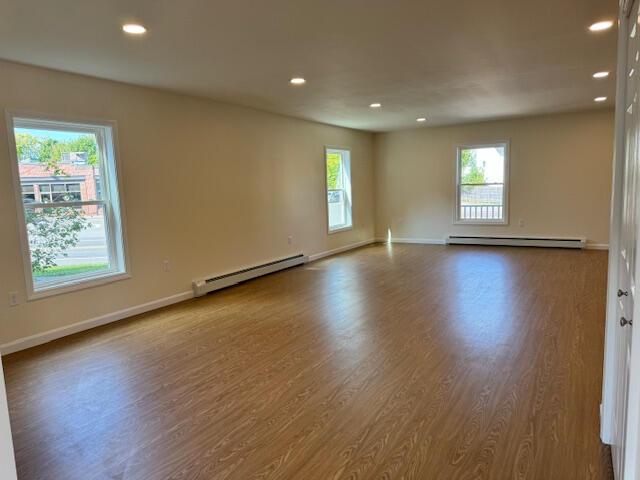 unfurnished room with a wealth of natural light, baseboard heating, and hardwood / wood-style flooring