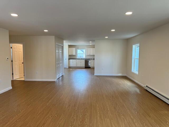 unfurnished living room with wood-type flooring, baseboard heating, and sink