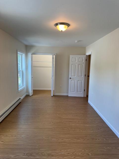 unfurnished bedroom with a baseboard heating unit, a closet, and hardwood / wood-style floors