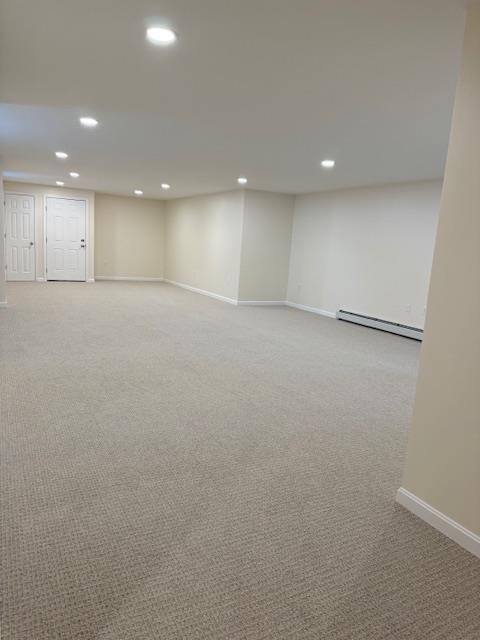 basement with baseboard heating and light colored carpet