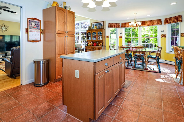 kitchen with pendant lighting, ceiling fan with notable chandelier, a kitchen island, and dark tile patterned floors