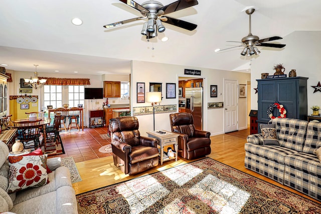 living room featuring ceiling fan with notable chandelier, light hardwood / wood-style floors, and vaulted ceiling