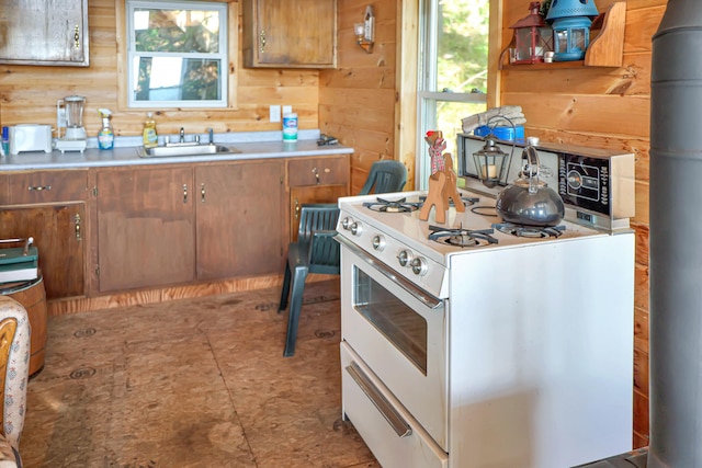 kitchen featuring white range with gas cooktop, sink, and wooden walls