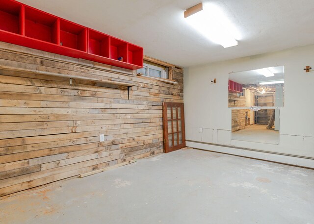 basement featuring a baseboard radiator and wooden walls