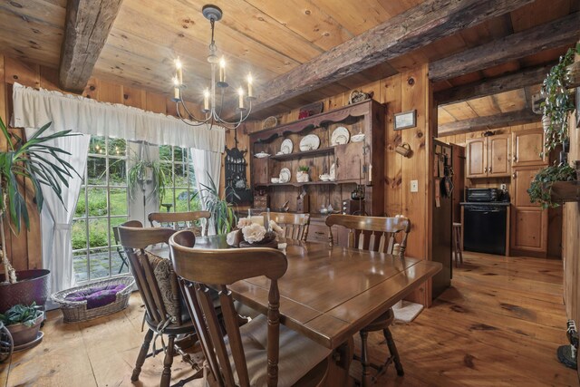 dining room with wood walls, an inviting chandelier, beamed ceiling, wooden ceiling, and light hardwood / wood-style flooring