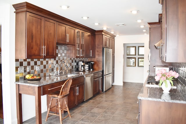 kitchen with sink, tasteful backsplash, stainless steel appliances, a breakfast bar, and dark stone counters