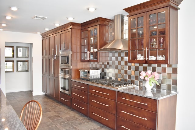 kitchen featuring wall chimney exhaust hood, backsplash, appliances with stainless steel finishes, and stone countertops