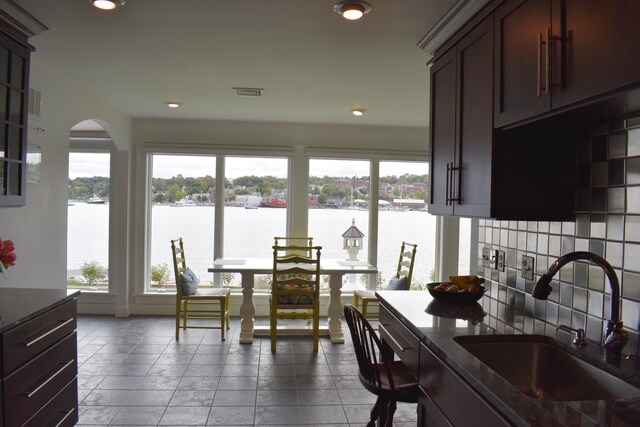 kitchen with a water view, backsplash, dark brown cabinetry, and sink