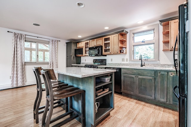 kitchen with black appliances, light stone countertops, light hardwood / wood-style flooring, and a kitchen island