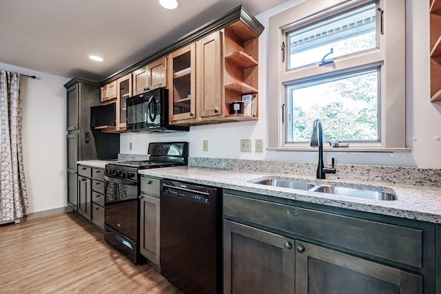 kitchen with light wood-type flooring, a wealth of natural light, black appliances, sink, and light stone countertops