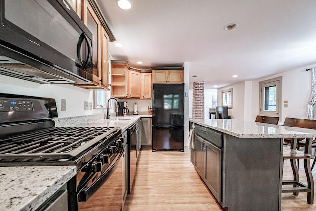 kitchen featuring a kitchen breakfast bar, black appliances, light hardwood / wood-style floors, sink, and light stone counters