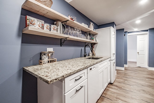 kitchen with light hardwood / wood-style flooring, light stone counters, sink, white dishwasher, and white cabinets