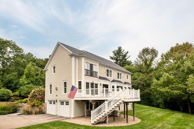 rear view of house with driveway, an attached garage, stairs, a deck, and a lawn