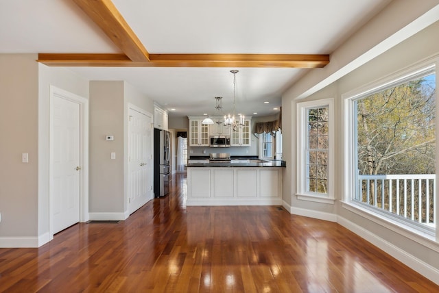 kitchen featuring dark countertops, beam ceiling, a peninsula, a notable chandelier, and stainless steel appliances