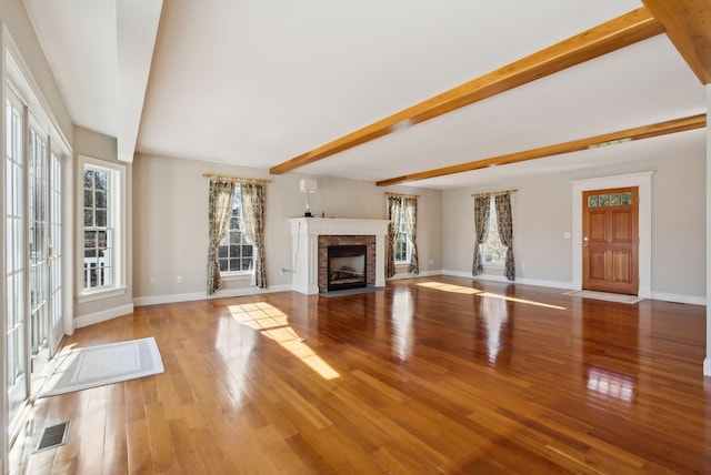 unfurnished living room with beamed ceiling, visible vents, a fireplace with flush hearth, hardwood / wood-style floors, and baseboards