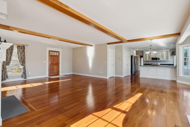 unfurnished living room featuring a wealth of natural light, beam ceiling, a chandelier, and dark wood finished floors