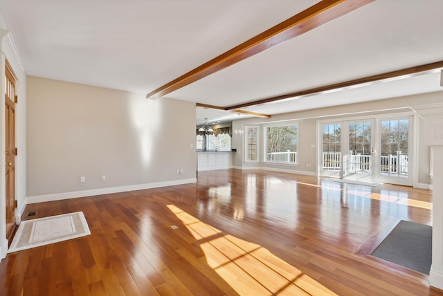 unfurnished living room featuring beamed ceiling, wood finished floors, baseboards, and a wealth of natural light