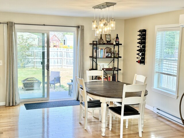 dining room with a baseboard radiator, light hardwood / wood-style floors, a notable chandelier, and a healthy amount of sunlight