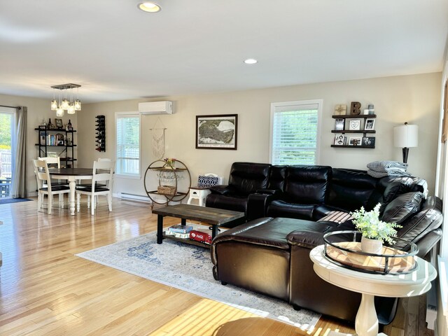 living room with a chandelier, a wealth of natural light, light hardwood / wood-style flooring, and an AC wall unit