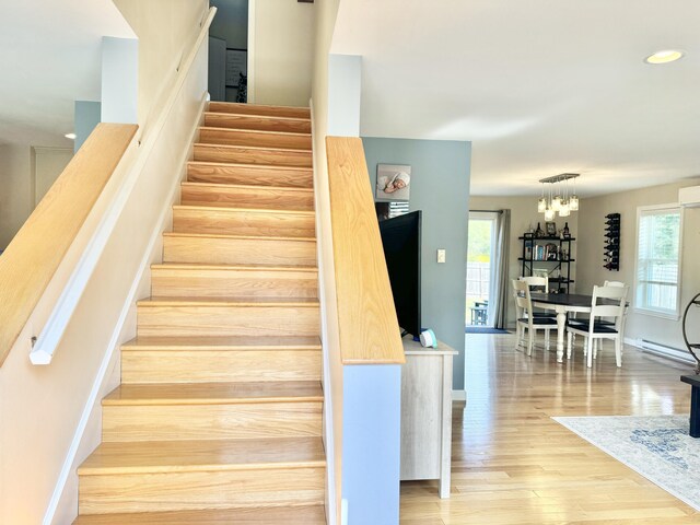 staircase with baseboard heating, hardwood / wood-style flooring, plenty of natural light, and a notable chandelier